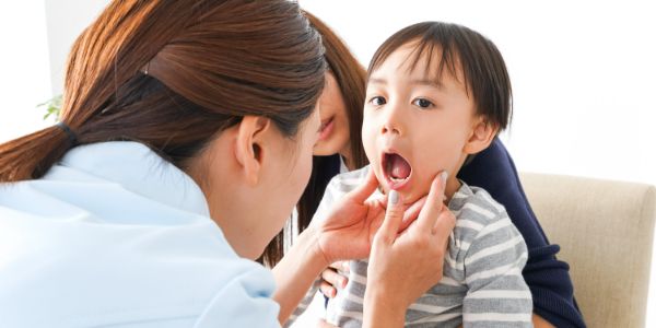 大きい口を開ける子供と診察する医師